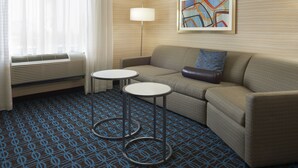 A hotel room with a sofa, two round tables, a lamp, a framed abstract painting, and a patterned carpet. - Fairfield Inn & Suites by Marriott Barrie (Barrie)