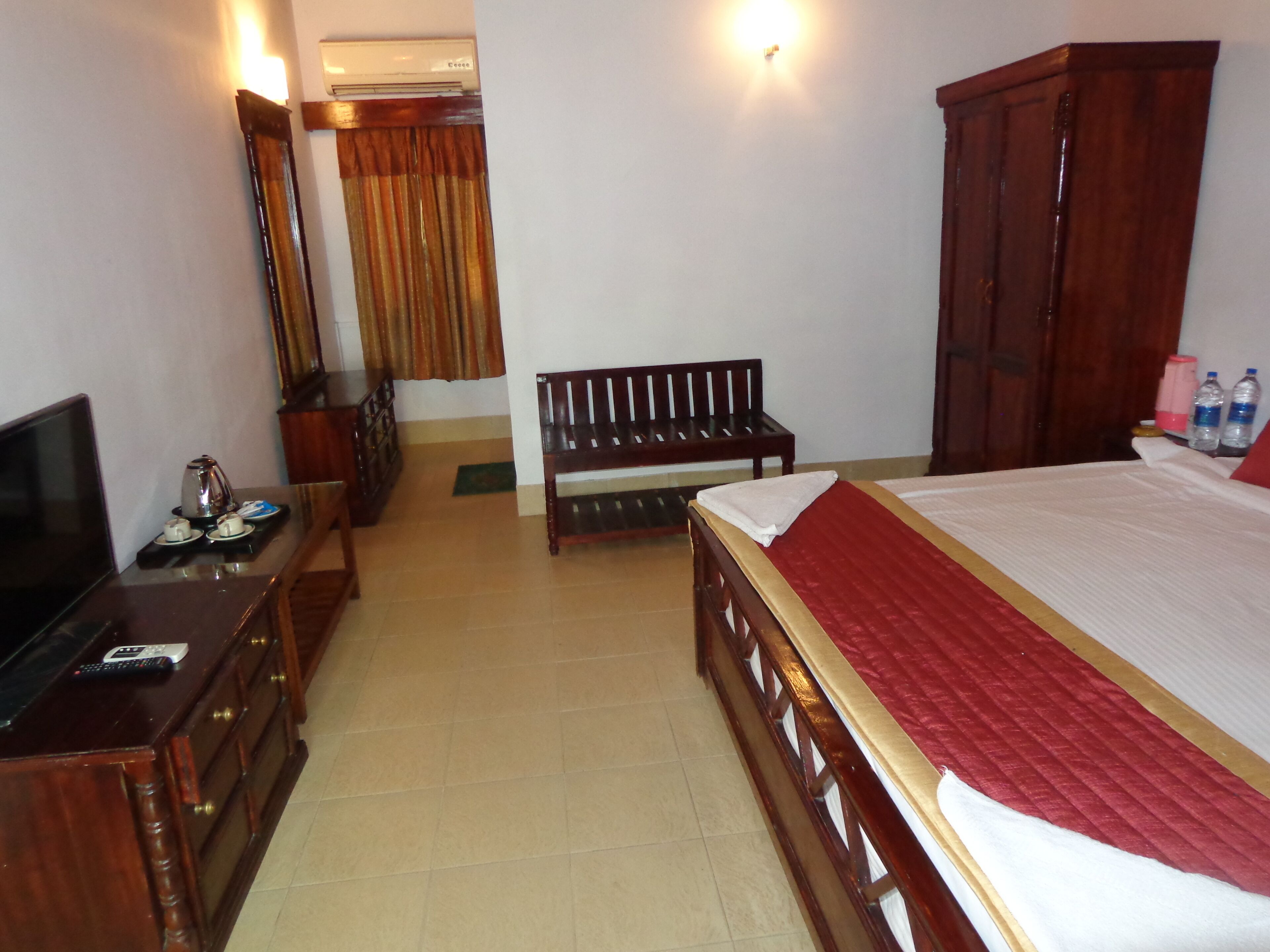 A hotel room with a bed, a wooden bench, a TV on a dresser, and a wardrobe.