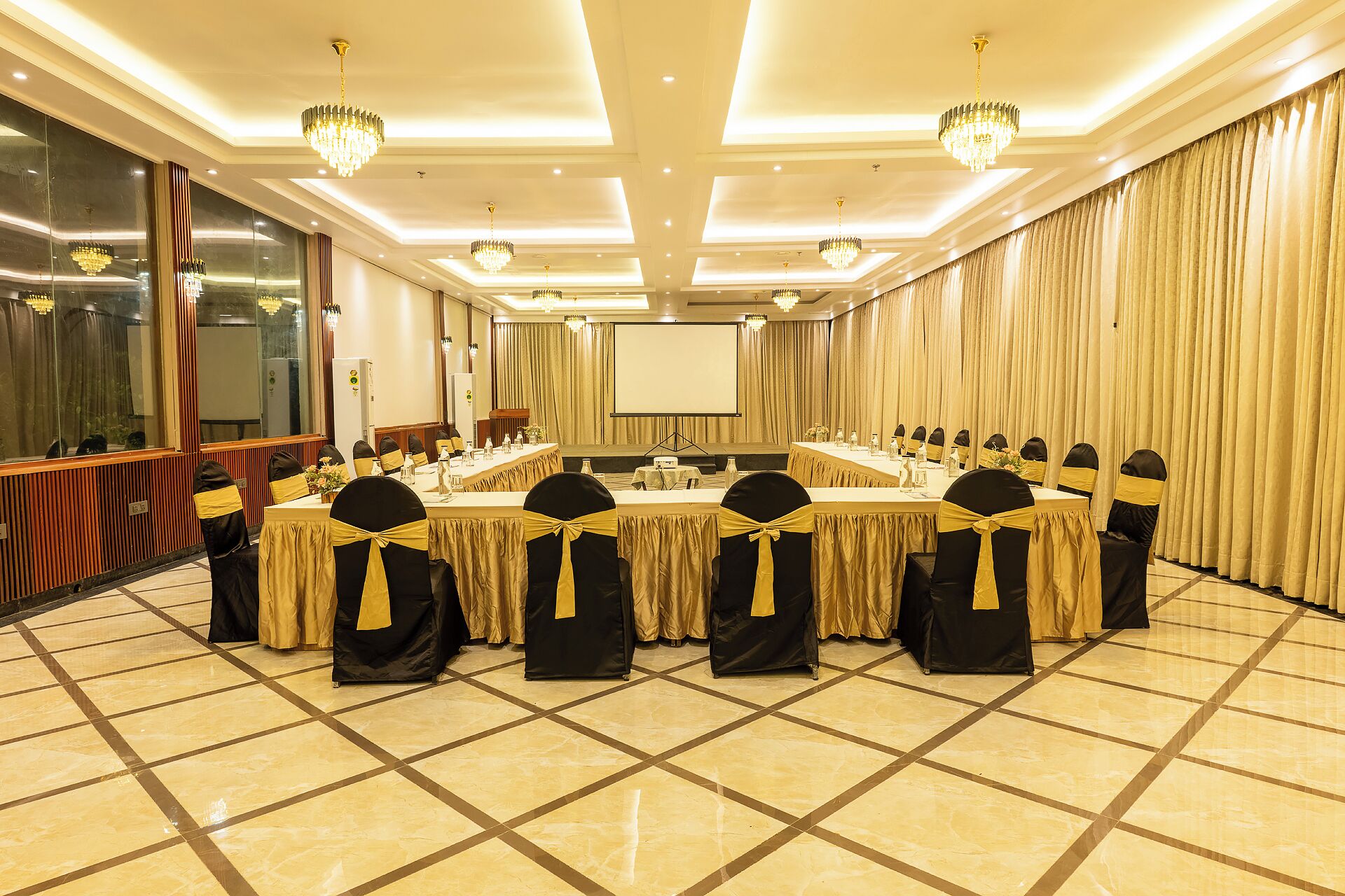 A conference room with a long table, chairs with yellow sashes, chandeliers, and a large screen.