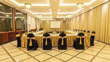 A conference room with a long table, chairs with yellow sashes, chandeliers, and a large screen.