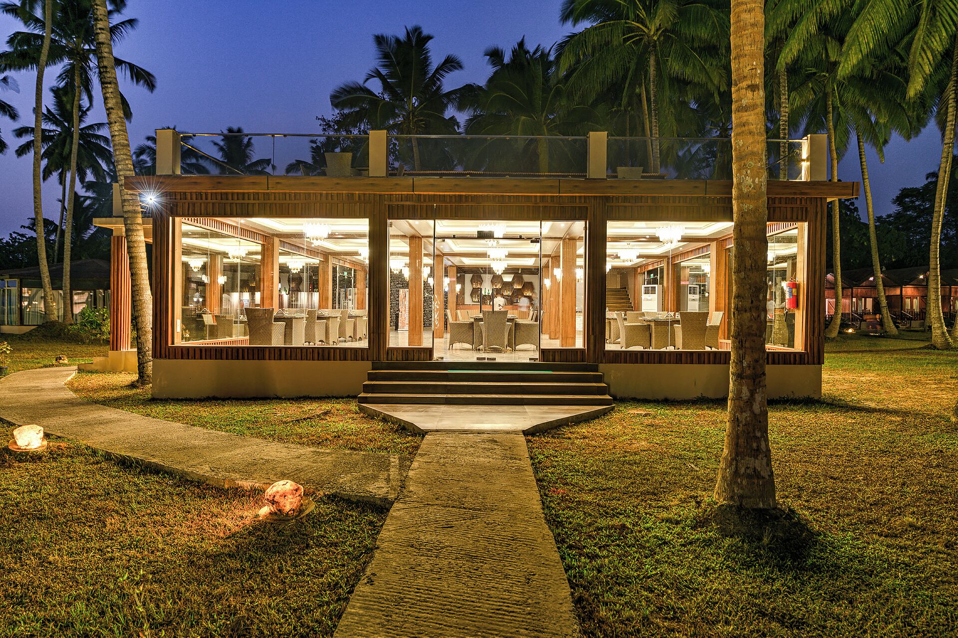 A modern, well-lit building with glass doors and windows, surrounded by palm trees.