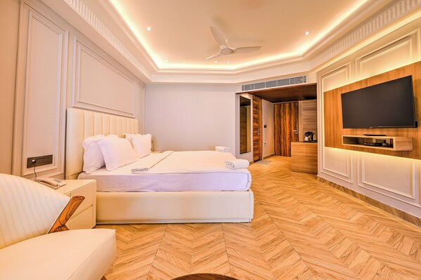 Una habitación de hotel moderna con una cama grande, un televisor de pantalla plana en la pared y suelo de madera.