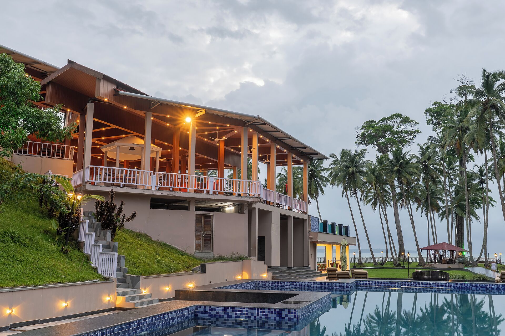 A resort with a swimming pool, a covered outdoor area with seating, and palm trees.