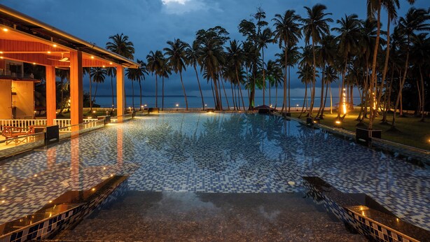 A swimming pool with tiled flooring, surrounded by palm trees and a view of the ocean. - Silver Sand Sea Princess Beach Resort (Ferrurgunj)