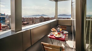 Ein Balkon mit Frühstückstisch, mit Blick auf eine Stadtlandschaft mit Gebäuden und einer fernen Bergkette.