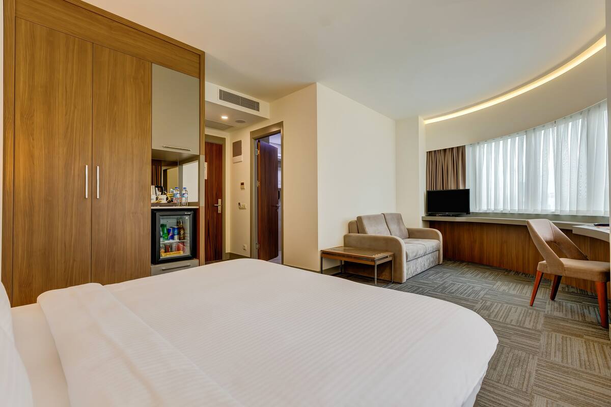 Une chambre d’hôtel avec un grand lit, un bureau avec une chaise, une télévision, un minibar et une armoire.