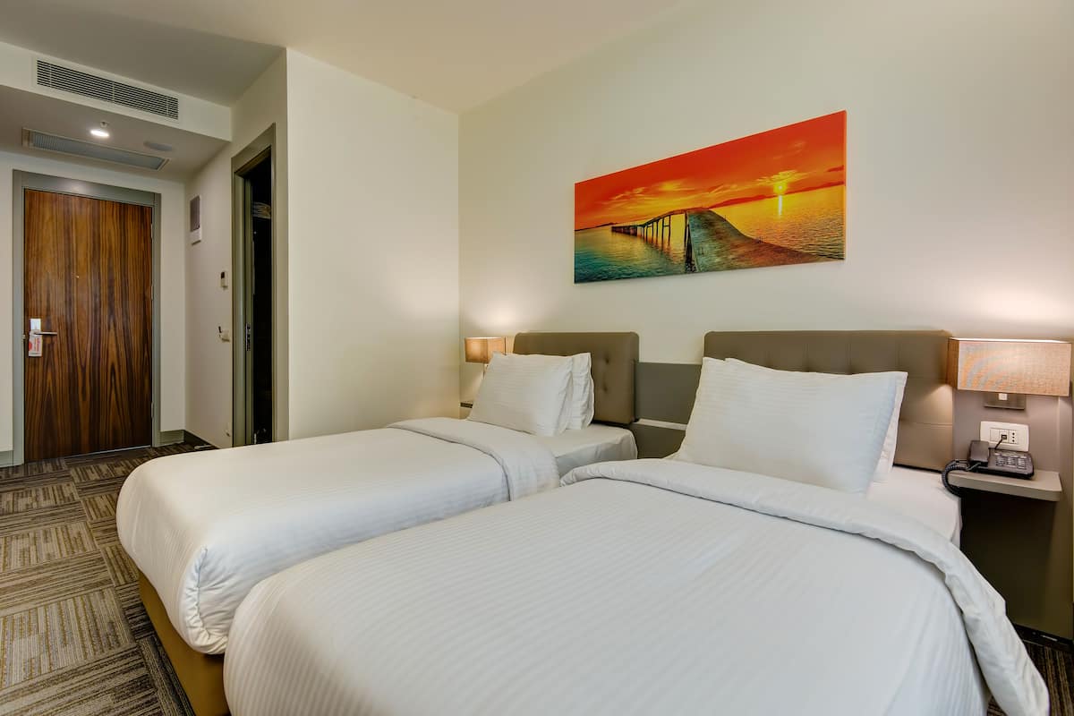 Une chambre d’hôtel avec deux lits, un tableau représentant un coucher de soleil, un téléphone sur la table de chevet et un sol recouvert de moquette.