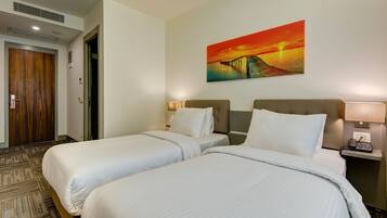 A hotel room with two beds, a painting of a sunset, a phone on the nightstand, and a carpeted floor.