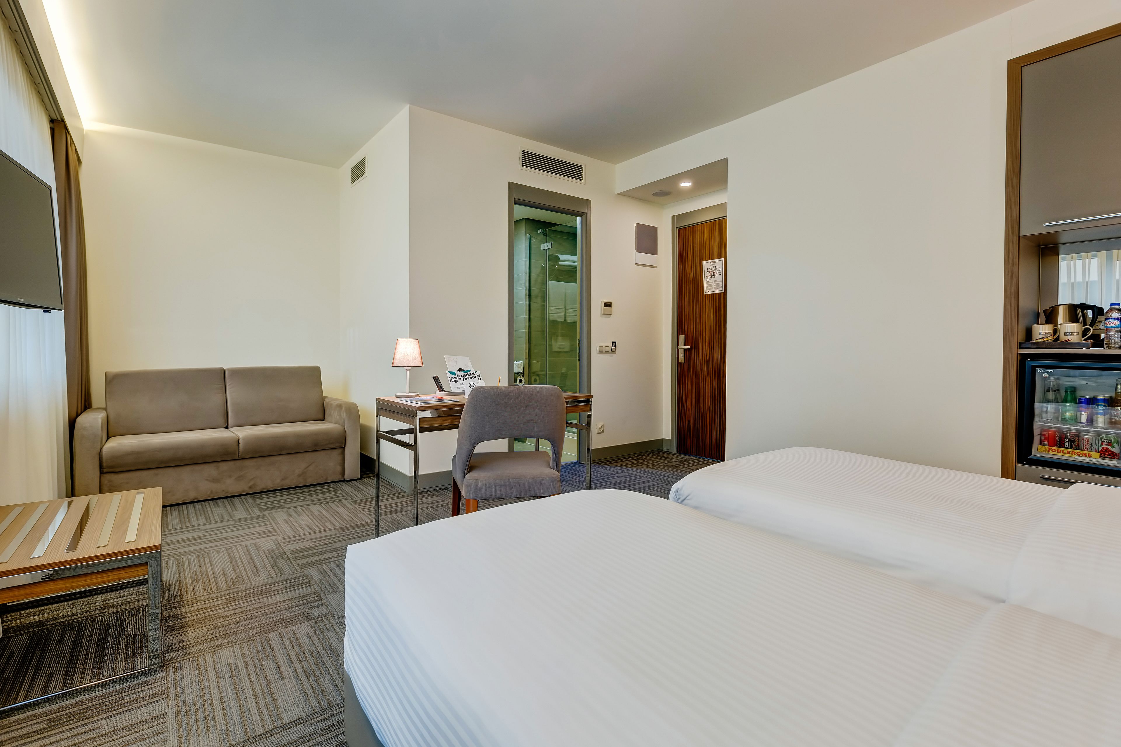 Een hotelkamer met een bed, een sofa, een bureau met een lamp, een stoel en een minibar.