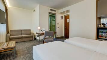 Een hotelkamer met een bed, een sofa, een bureau met een lamp, een stoel en een minibar.