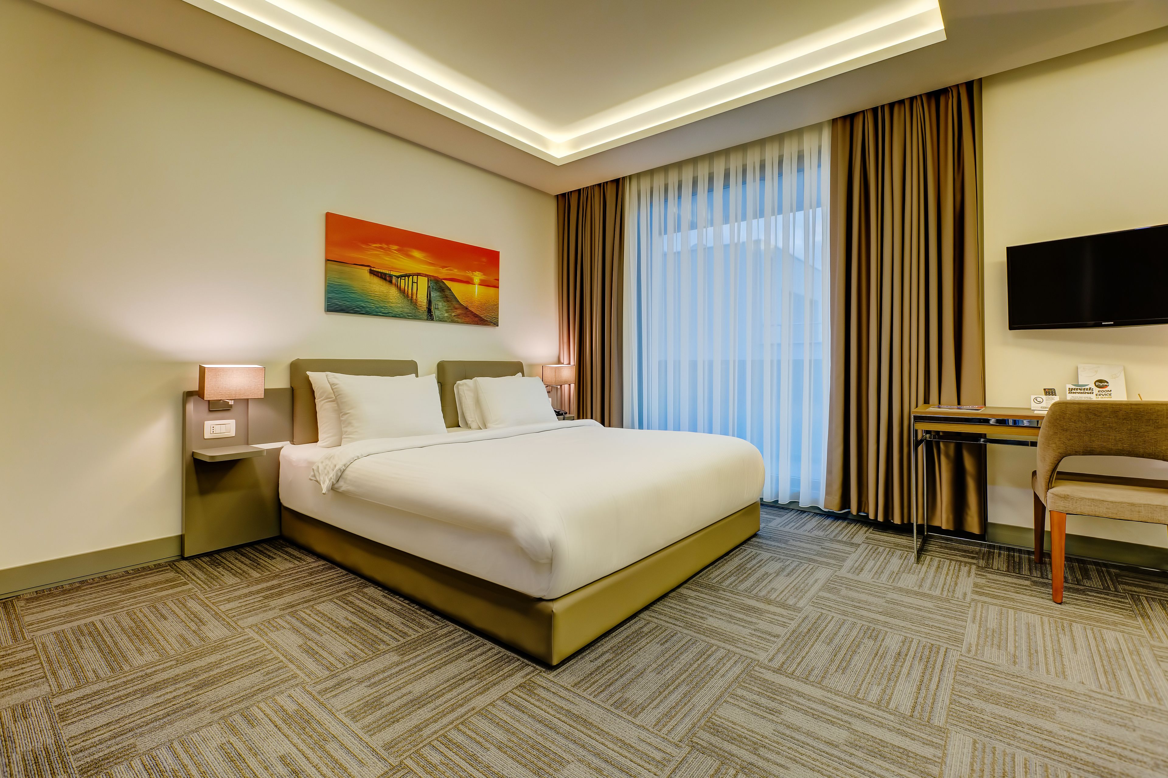 Hotelkamer met een groot bed, een bureau, een stoel, een flatscreen televisie en een schilderij aan de muur.