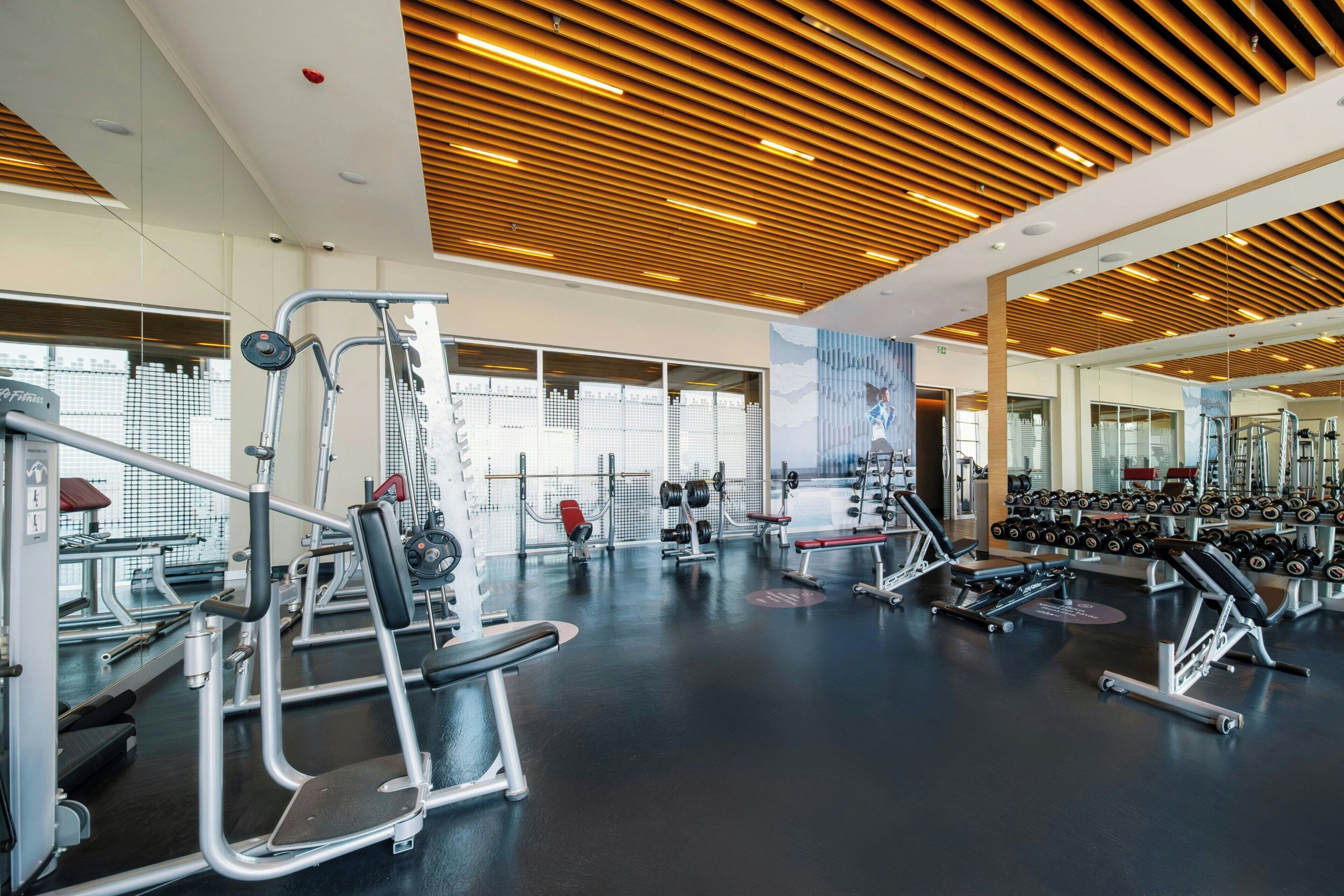 Un gimnasio con diversos equipos de ejercicio, ventanas amplias y techo de madera.