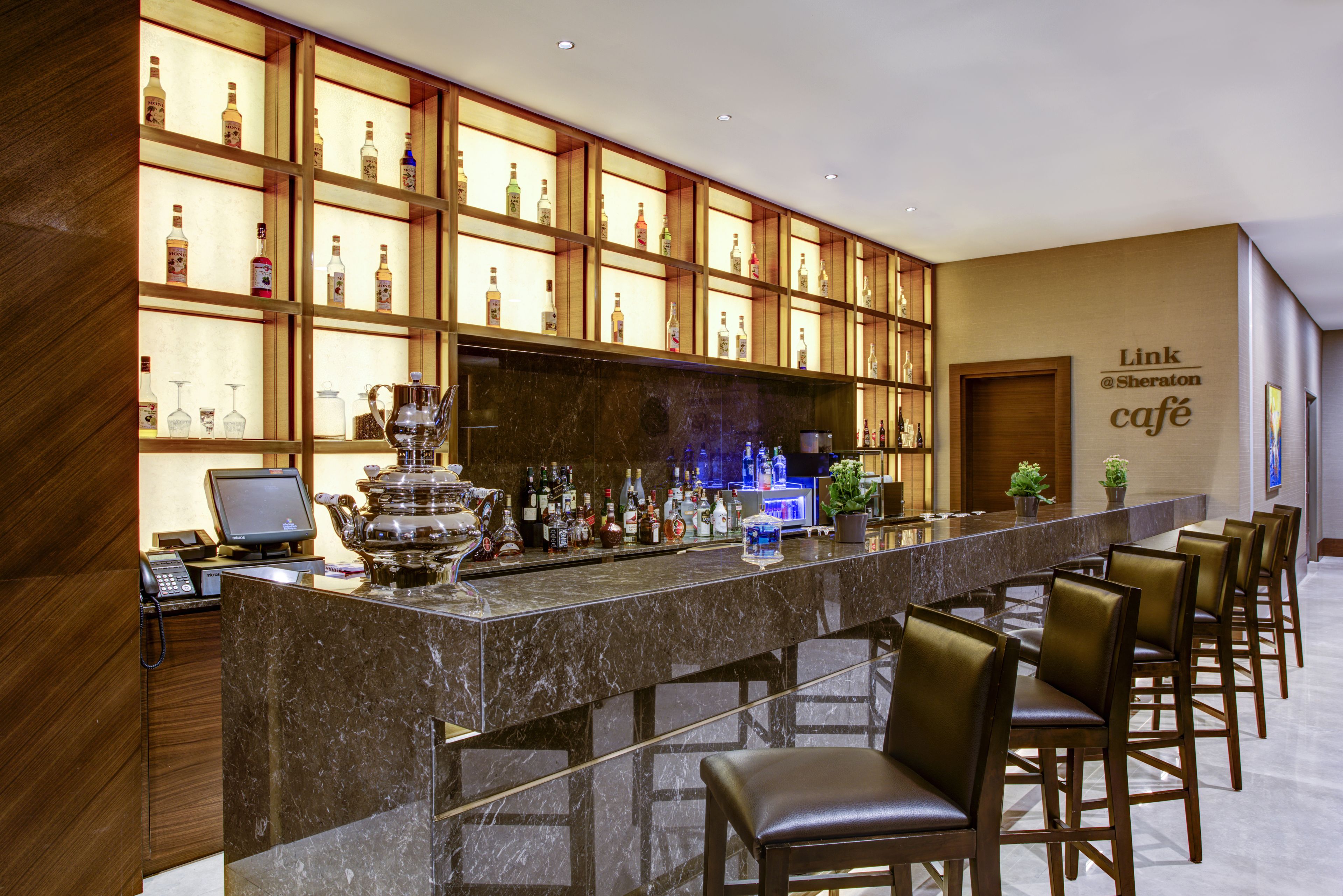A bar area with a long counter, multiple shelves of bottles, and several bar stools.