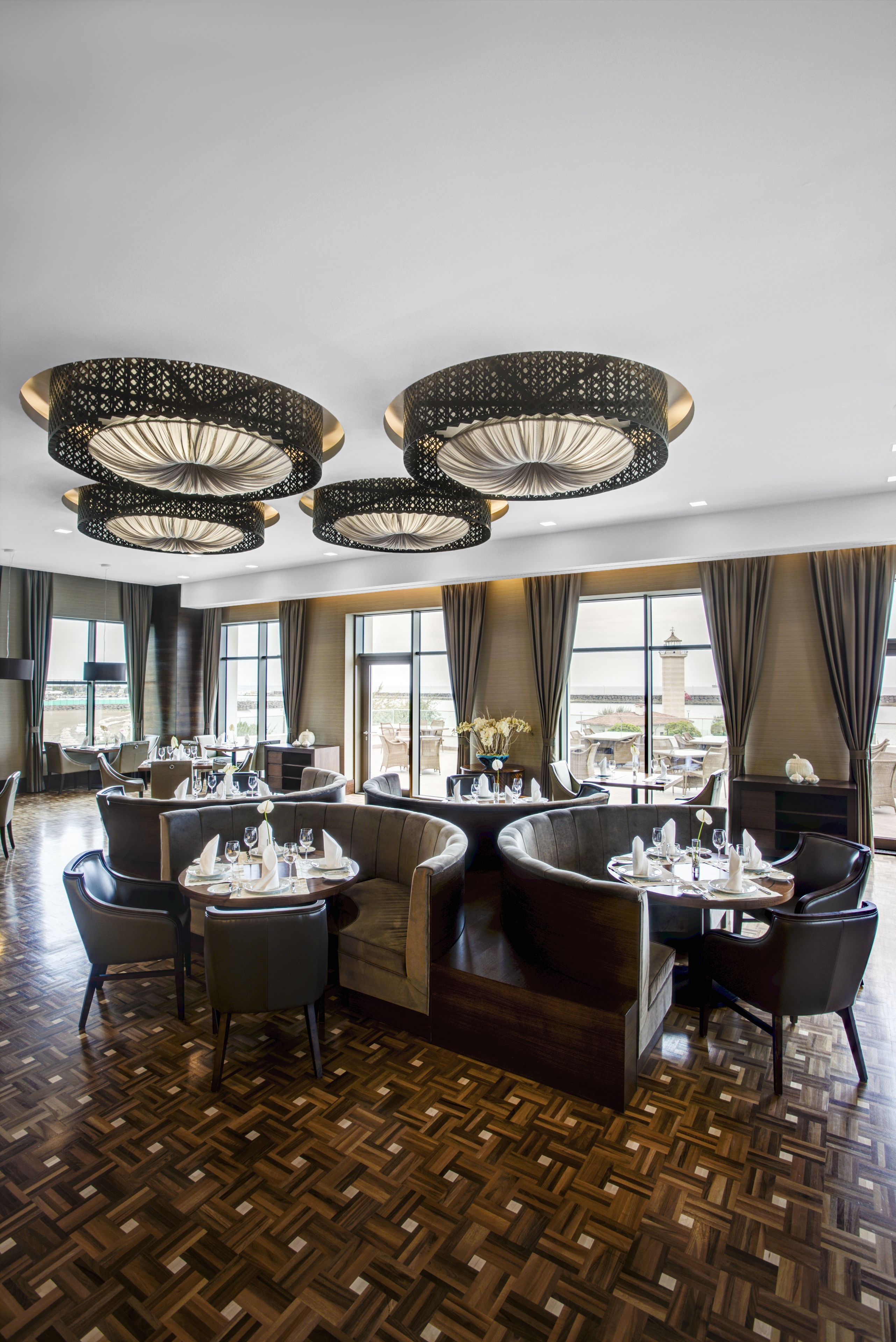 A spacious hotel lobby with a high ceiling, large windows, and a central seating area with tables set for dining.