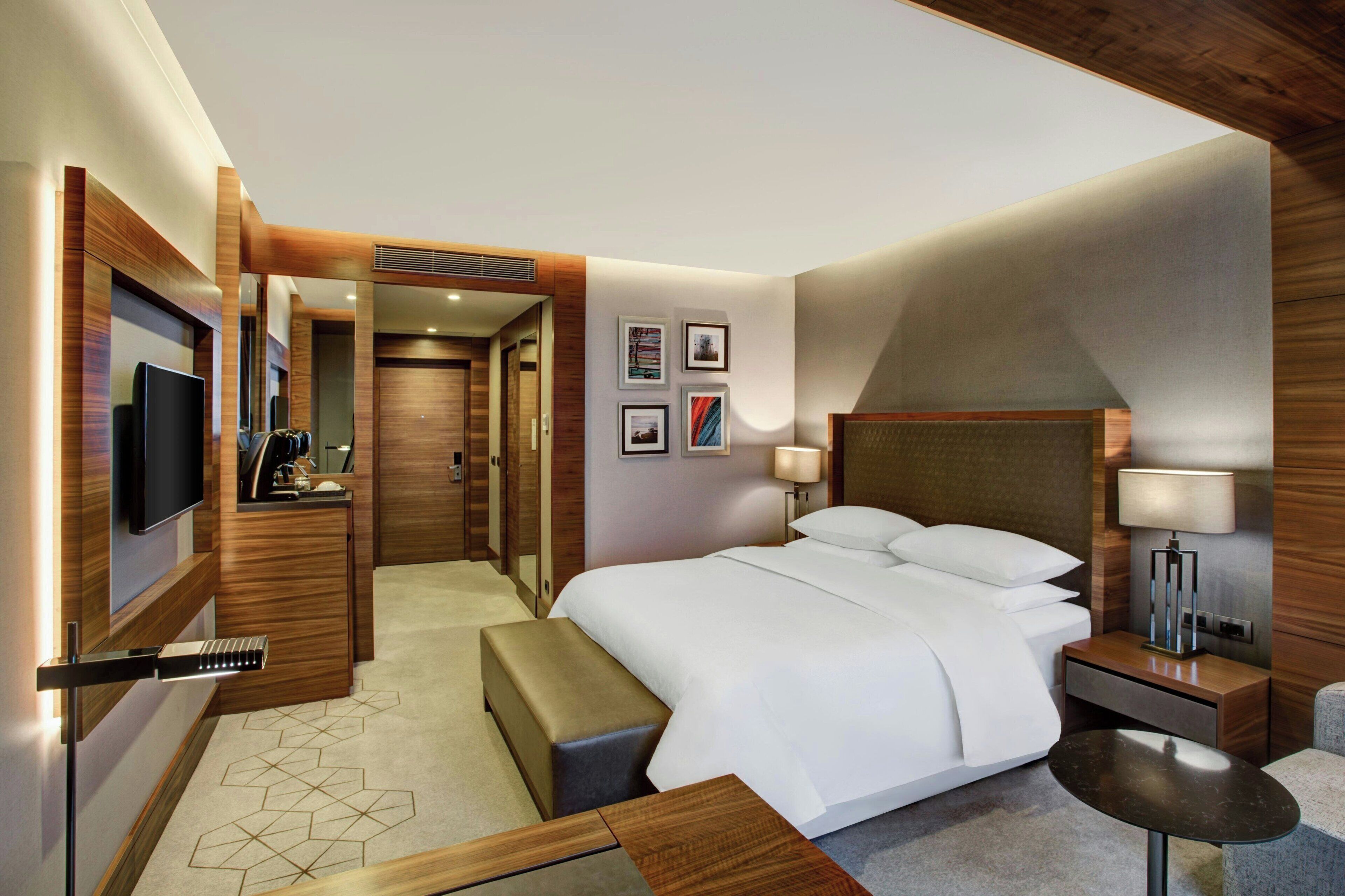 A modern hotel room with a large bed, a TV, a desk, and a mirror.