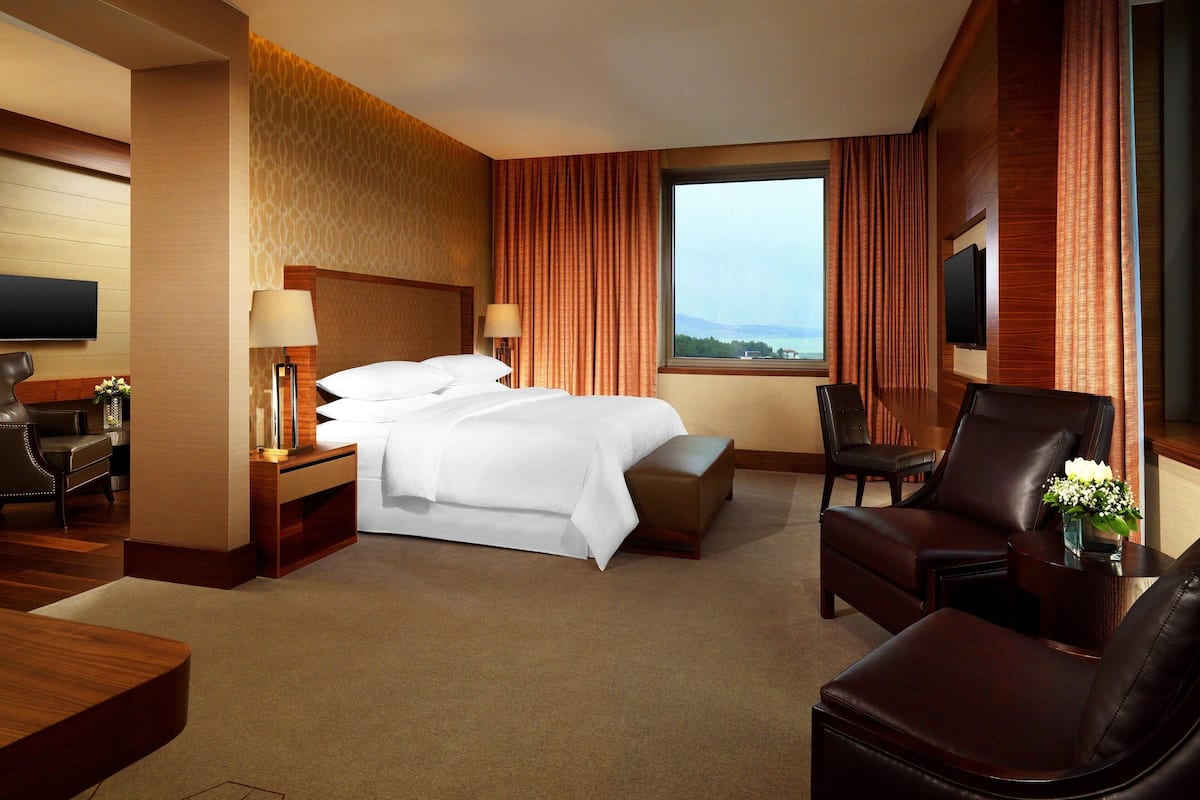Una habitación de hotel con una cama grande, un escritorio, una silla, un televisor y una ventana con cortinas.