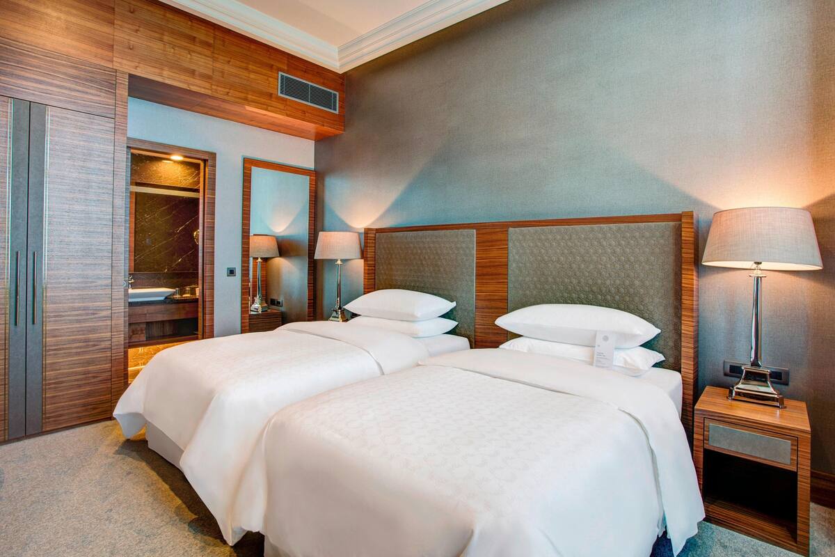 Una habitación de hotel con dos camas, un armario de madera, un espejo y una mesita de noche con lámpara.
