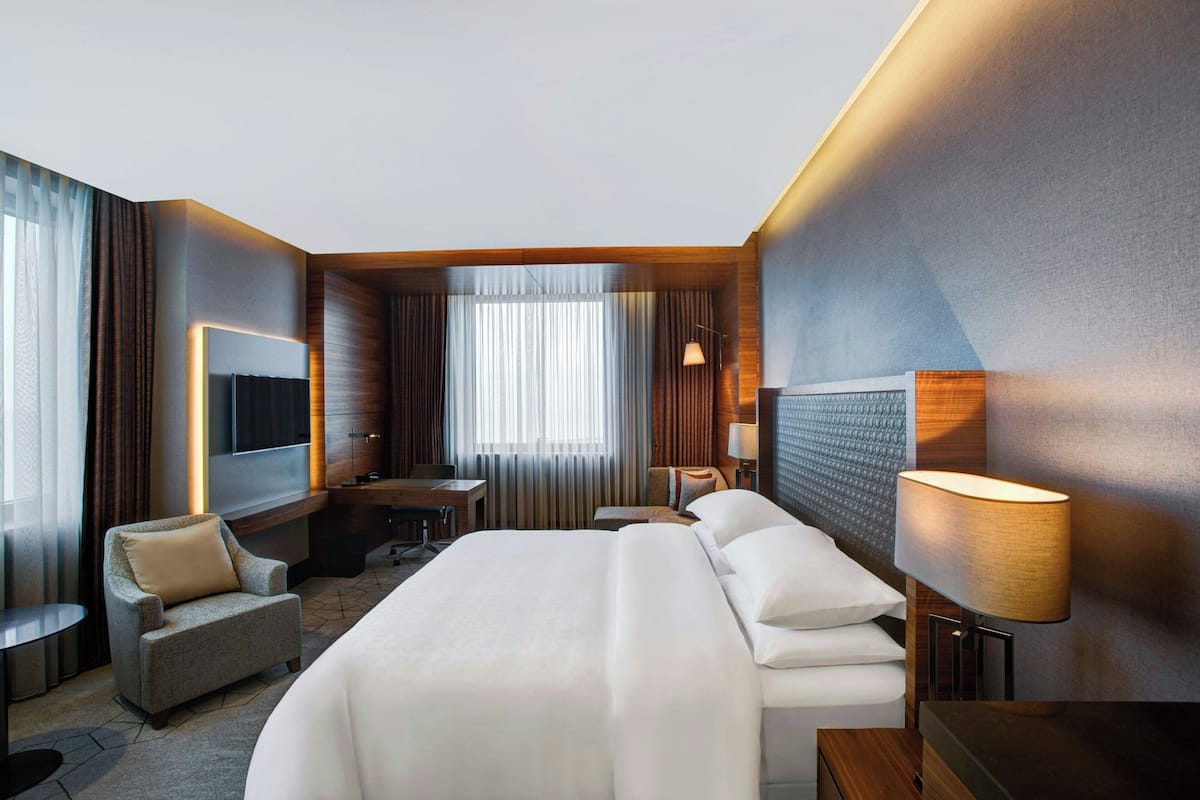 Una habitación de hotel moderna con una cama grande, un escritorio, una silla, un televisor y una lámpara.