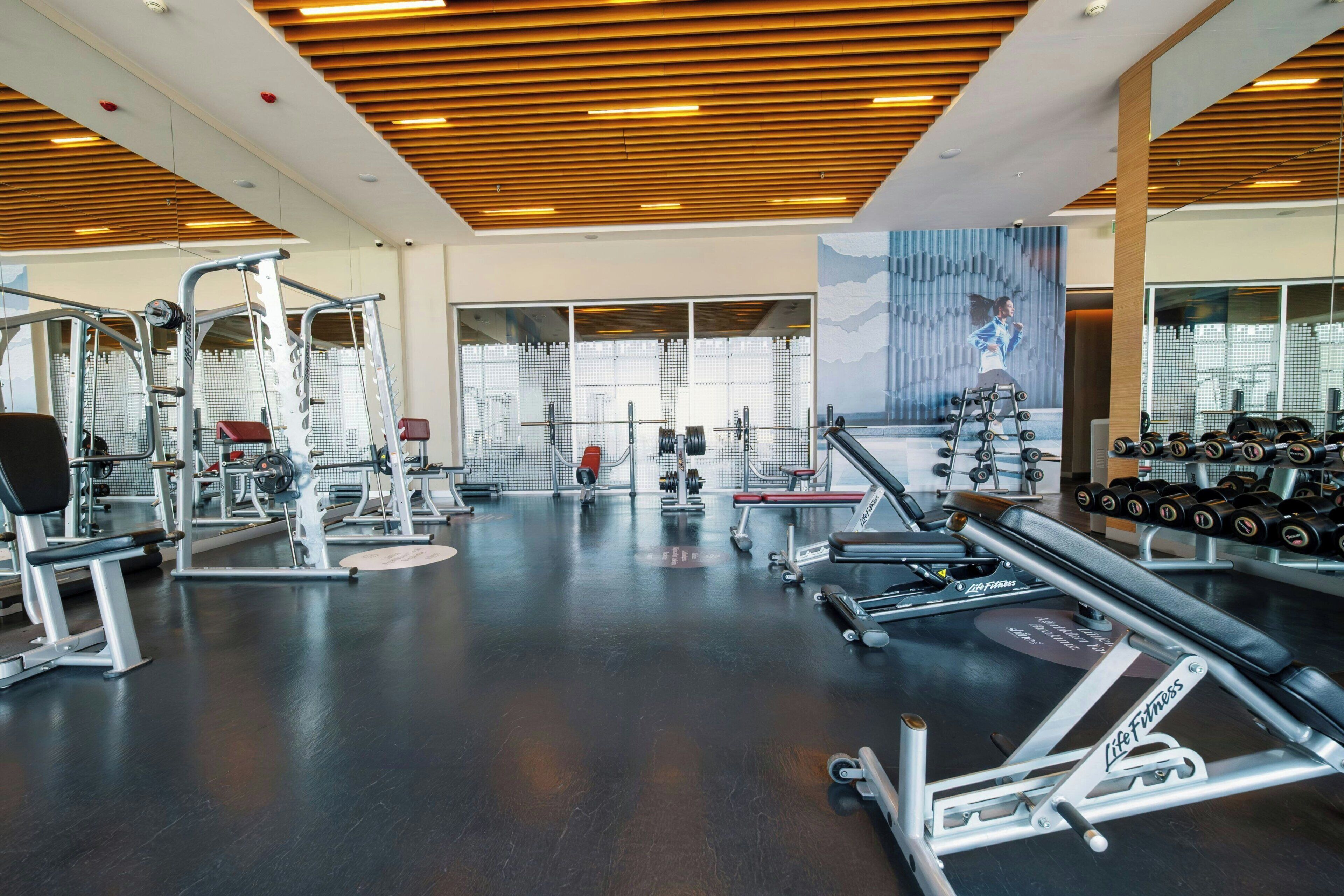 A gym with various exercise equipment, large windows, and a wooden ceiling.
