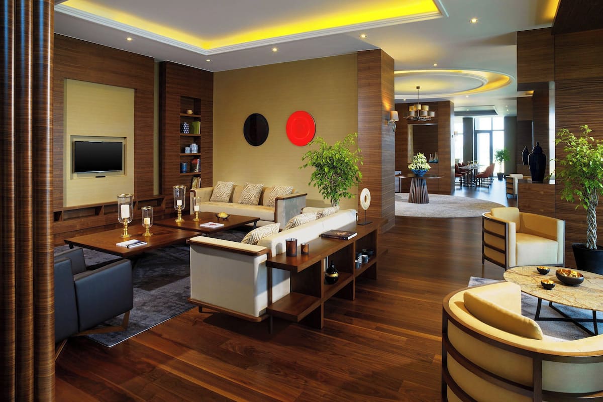 Una sala de estar moderna con un sofá, una mesa de centro y un televisor montado en la pared. Hay elementos decorativos y una planta en los estantes.