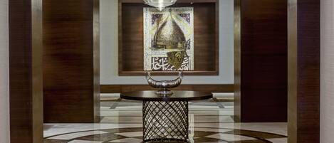 A lobby with a central table featuring a decorative metal base and a hanging lamp.