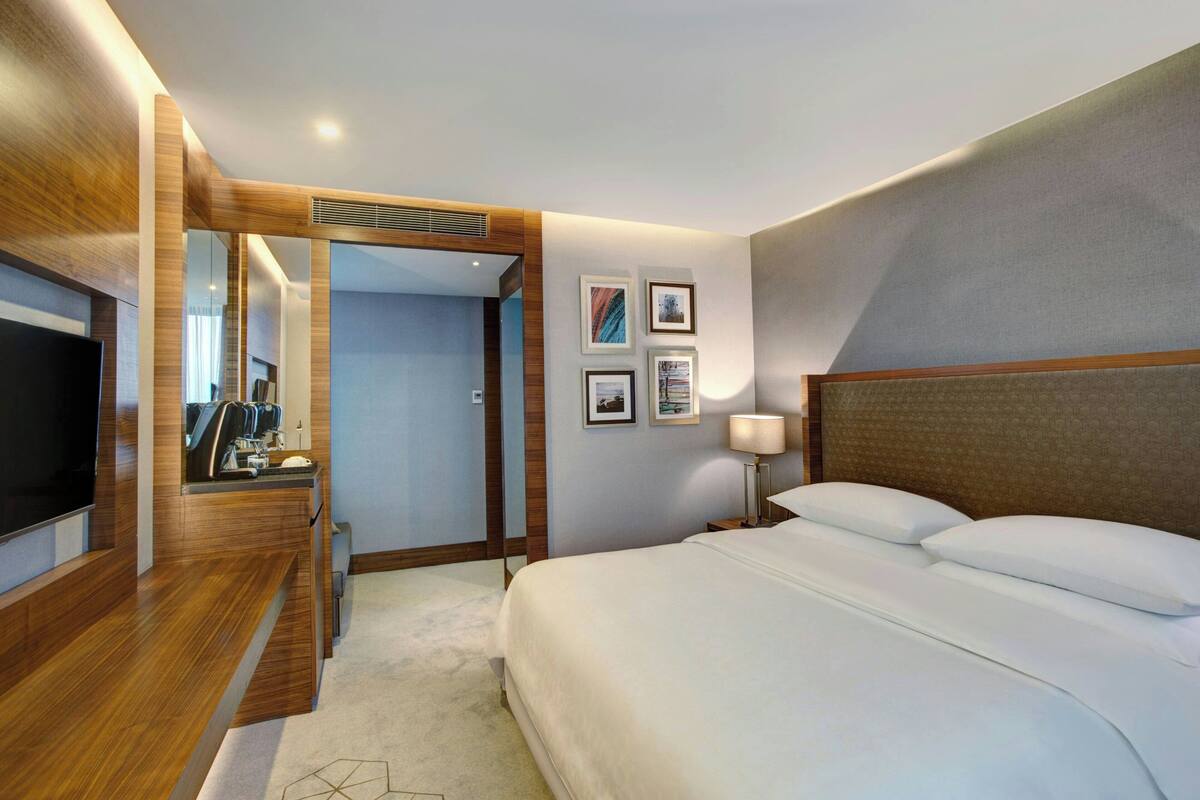 Una habitación de hotel con una cama grande, televisión, escritorio con cafetera y cuadros en la pared.