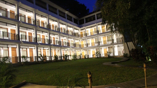 Un hotel de varios pisos con balcones, un césped cuidado y un camino empedrado.