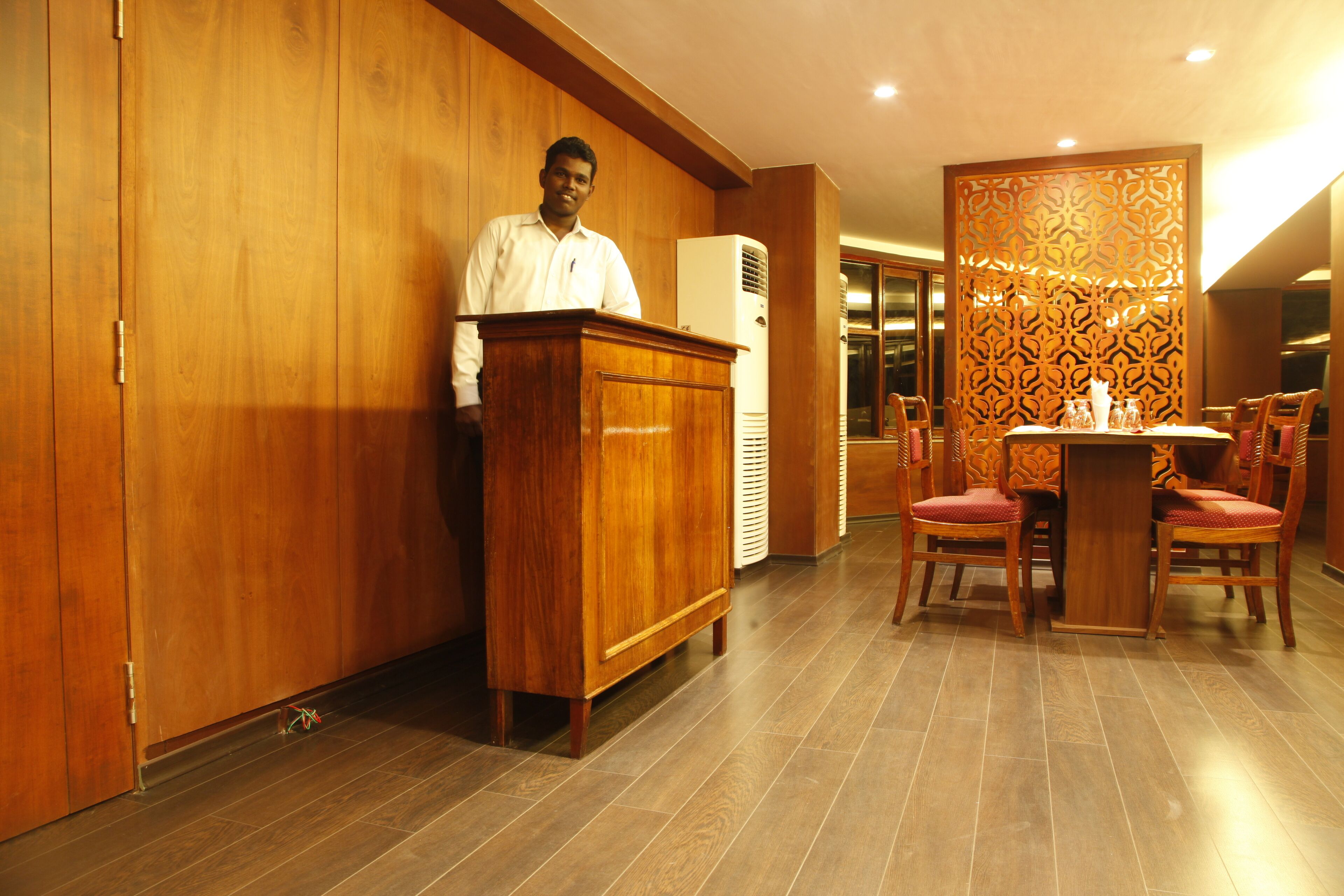 A wooden-paneled room with a podium, a dining table with chairs, and a patterned partition.