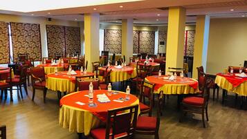 Un'ampia sala da pranzo con diversi tavoli rotondi ricoperti da tovaglie rosse, sedie in legno e una parete decorata sullo sfondo.