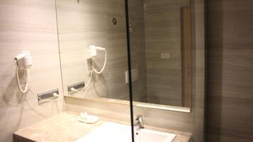 Casa de banho com bancada de mármore, lavatório branco, chuveiro manual e um espelho grande.
