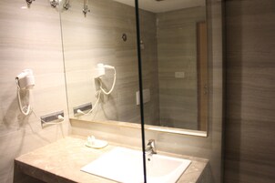 Casa de banho com bancada de mármore, lavatório branco, chuveiro manual e um espelho grande.