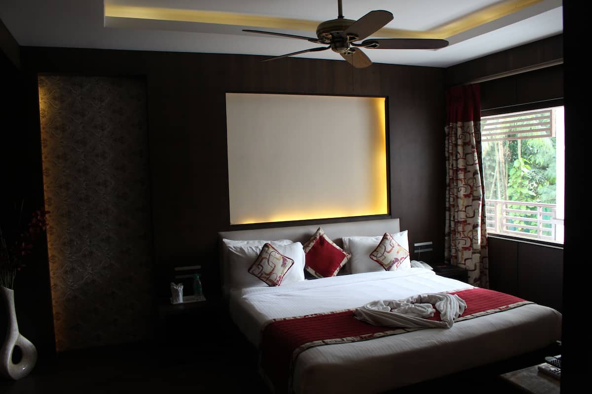 A hotel room with a bed, a ceiling fan, a nightstand, and a window with curtains.