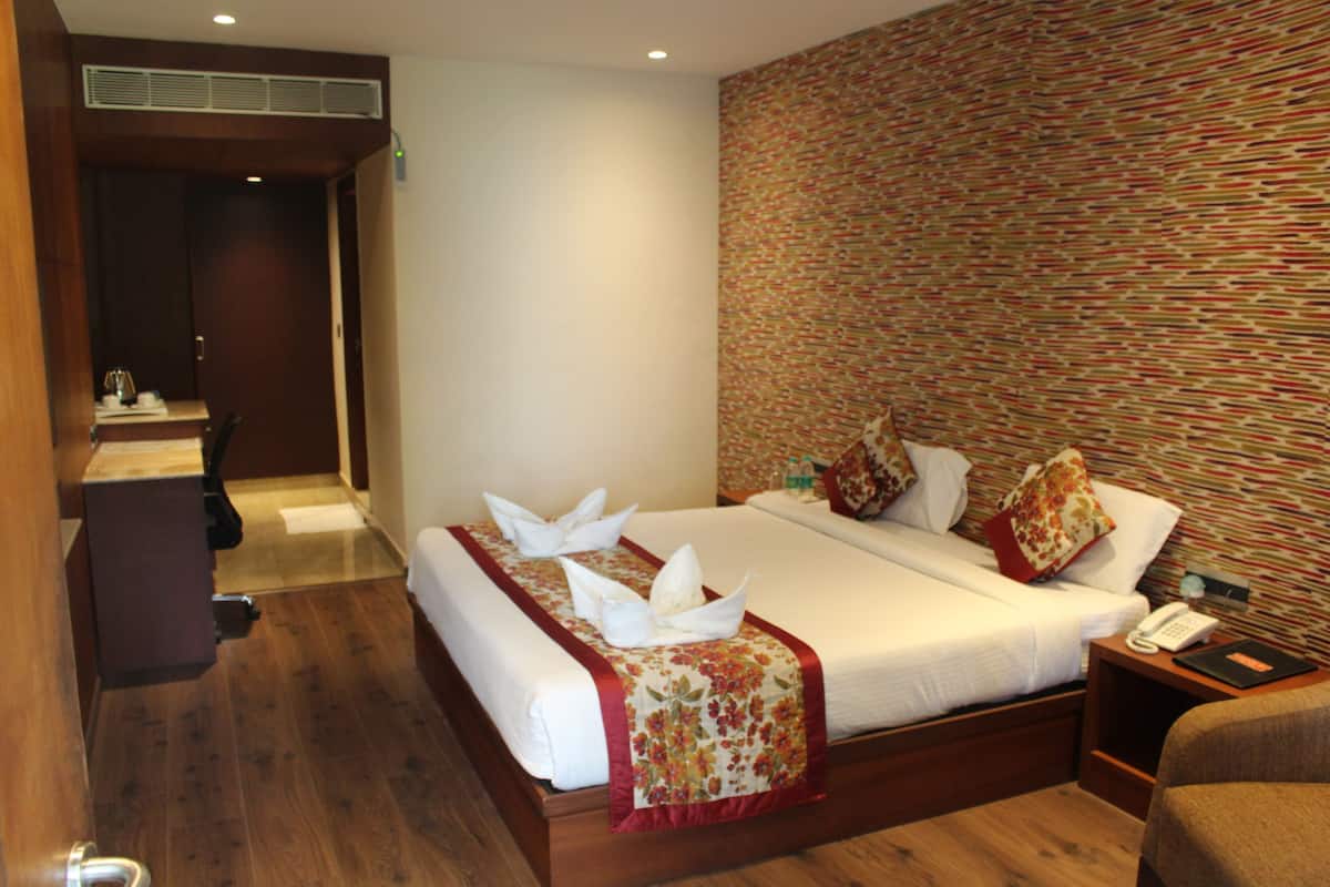 A hotel room with a wooden floor, a bed with white linens and red floral bedspread, a nightstand with a phone, and a patterned wall.