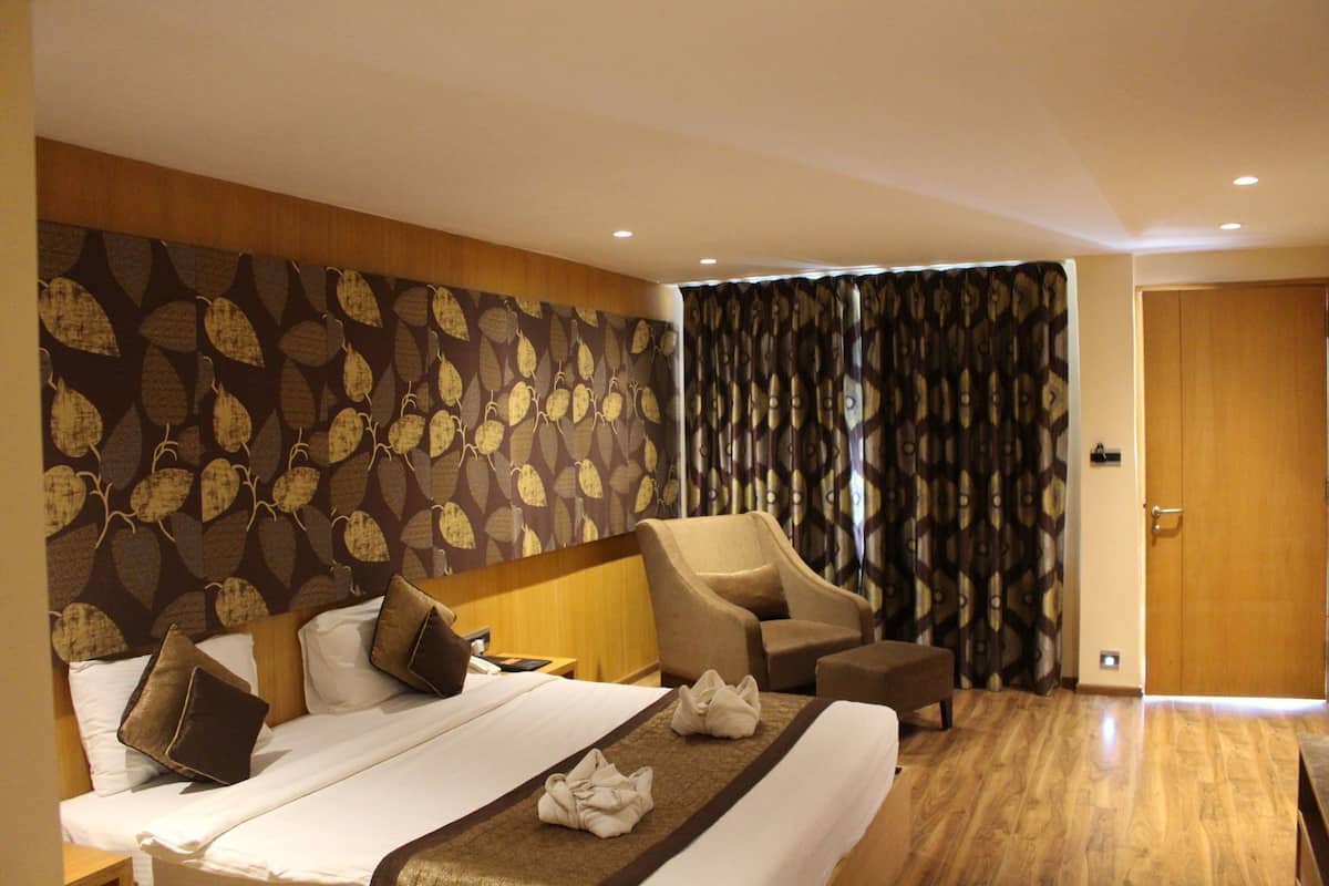 A hotel room with a bed, two armchairs, a wooden floor, and patterned wallpaper.