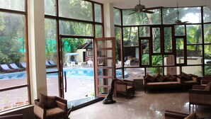 Amplio espacio interior con ventanas grandes, un ventilador de techo y vistas a una piscina al aire libre.