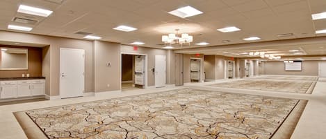 Amplia habitación de hotel vacía con alfombra estampada, varias puertas y un candelabro.