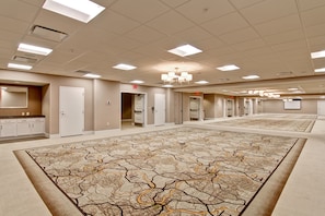 A large, empty hotel room with a patterned carpet, multiple doors, and a chandelier.
