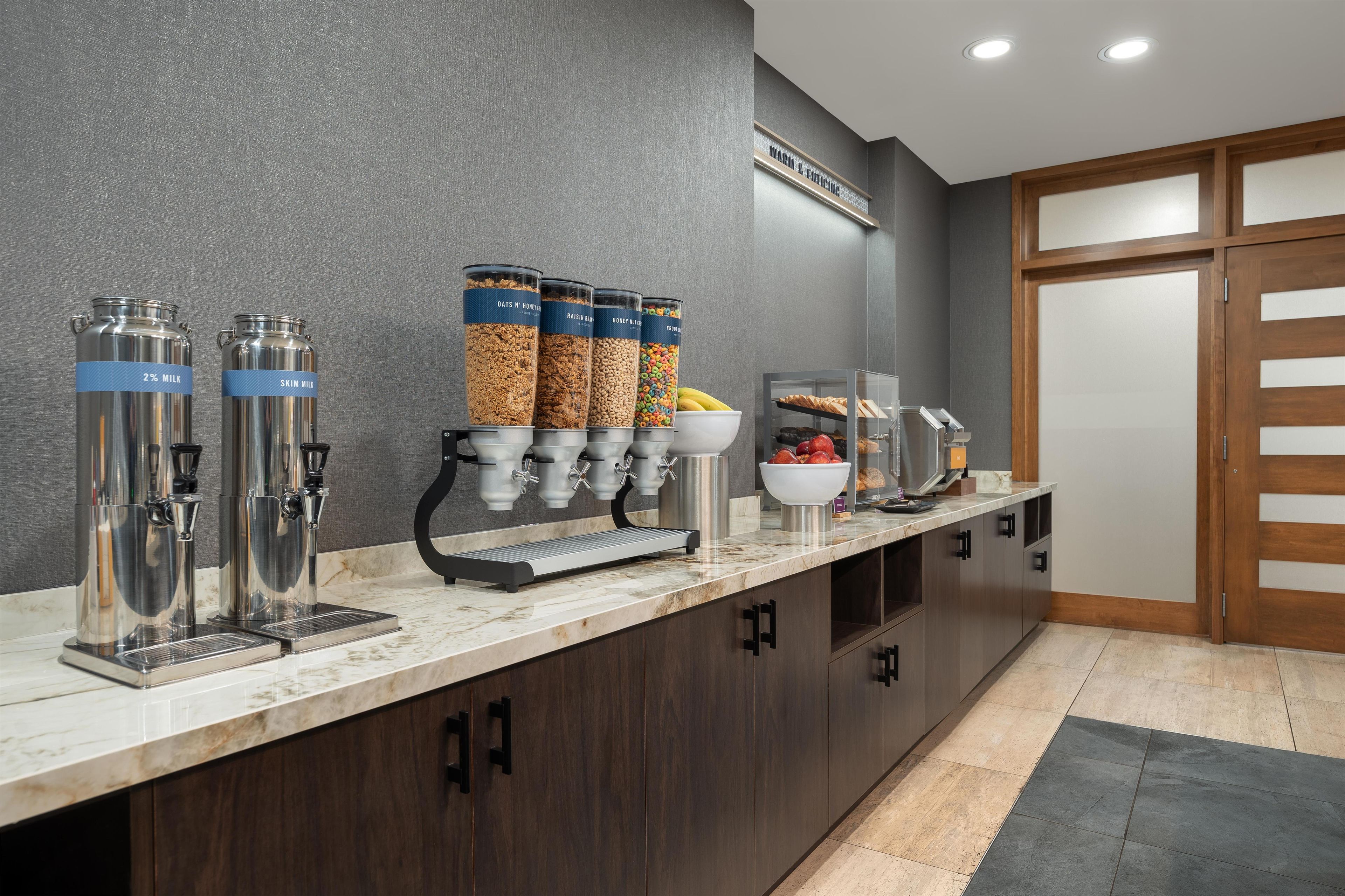 A self-service breakfast bar with dispensers and containers of milk, cereal, and fruits.