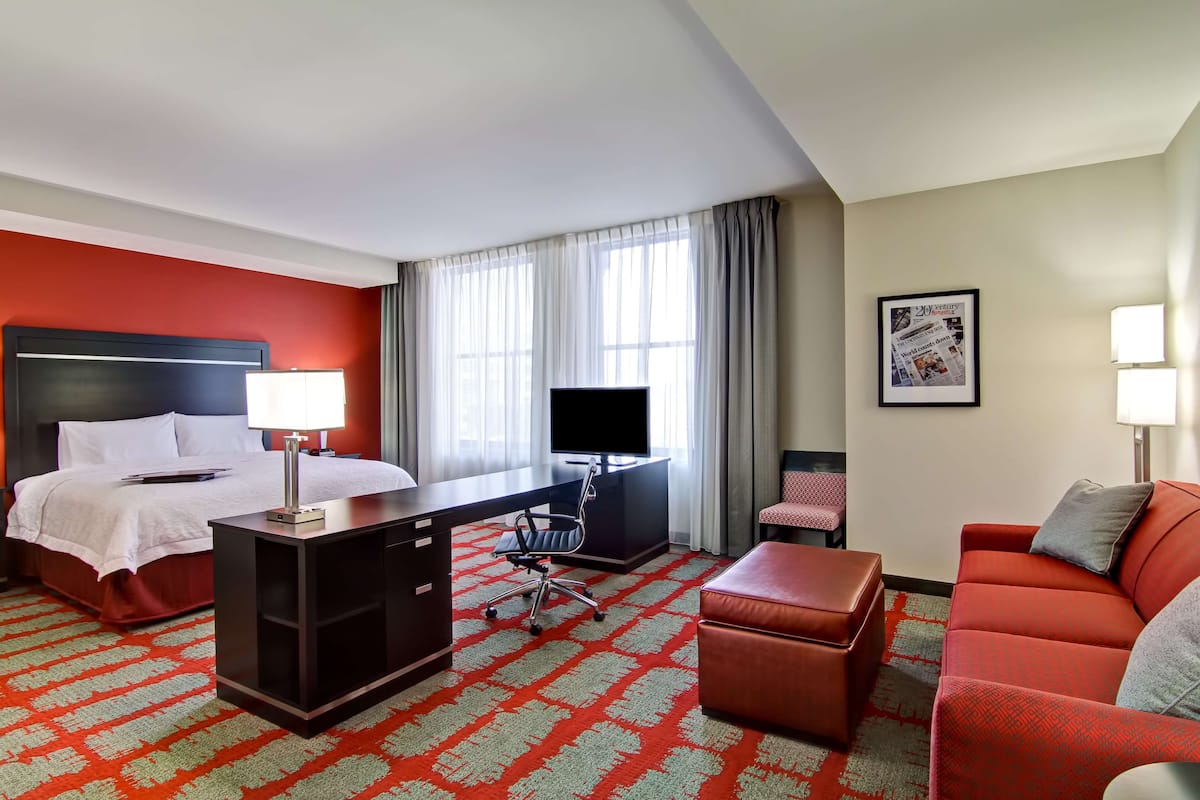 A hotel room with a bed, desk, office chair, and a red sofa.