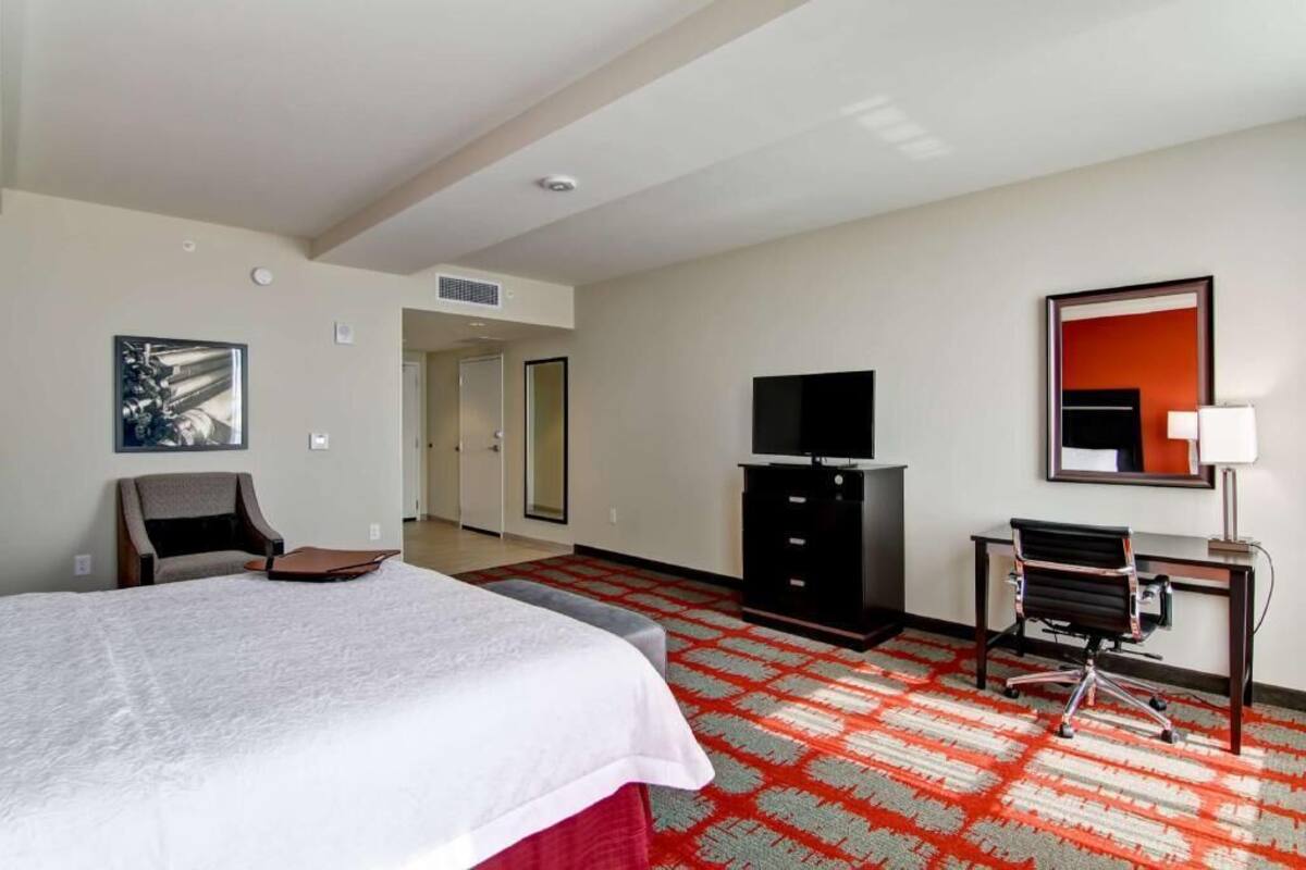 A hotel room with a bed, a desk with a chair, a television, and a mirror.