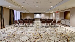 Un salón de conferencias con una pantalla grande, filas de sillas y una alfombra estampada.