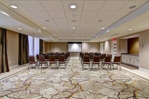 A conference room with a large screen, rows of chairs, and a patterned carpet. - Hampton Inn & Suites Cincinnati-Downtown (Cincinnati)