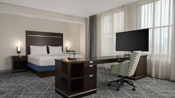 Habitación de hotel con cama, escritorio, silla, televisor y cortinas.