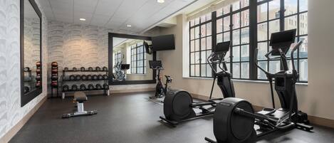 A gym with exercise equipment, a mirror, and a wall of dumbbells.