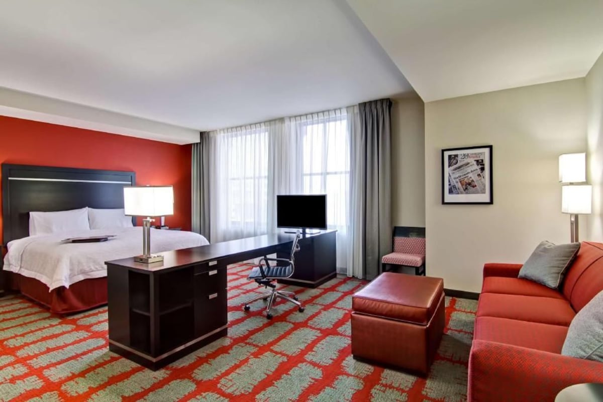 A hotel room with a bed, desk, office chair, red sofa, and a television.