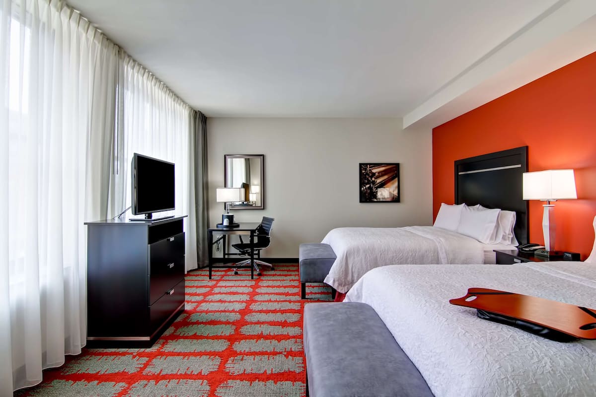 A hotel room with two beds, a desk with a chair, a television, and a red carpet.