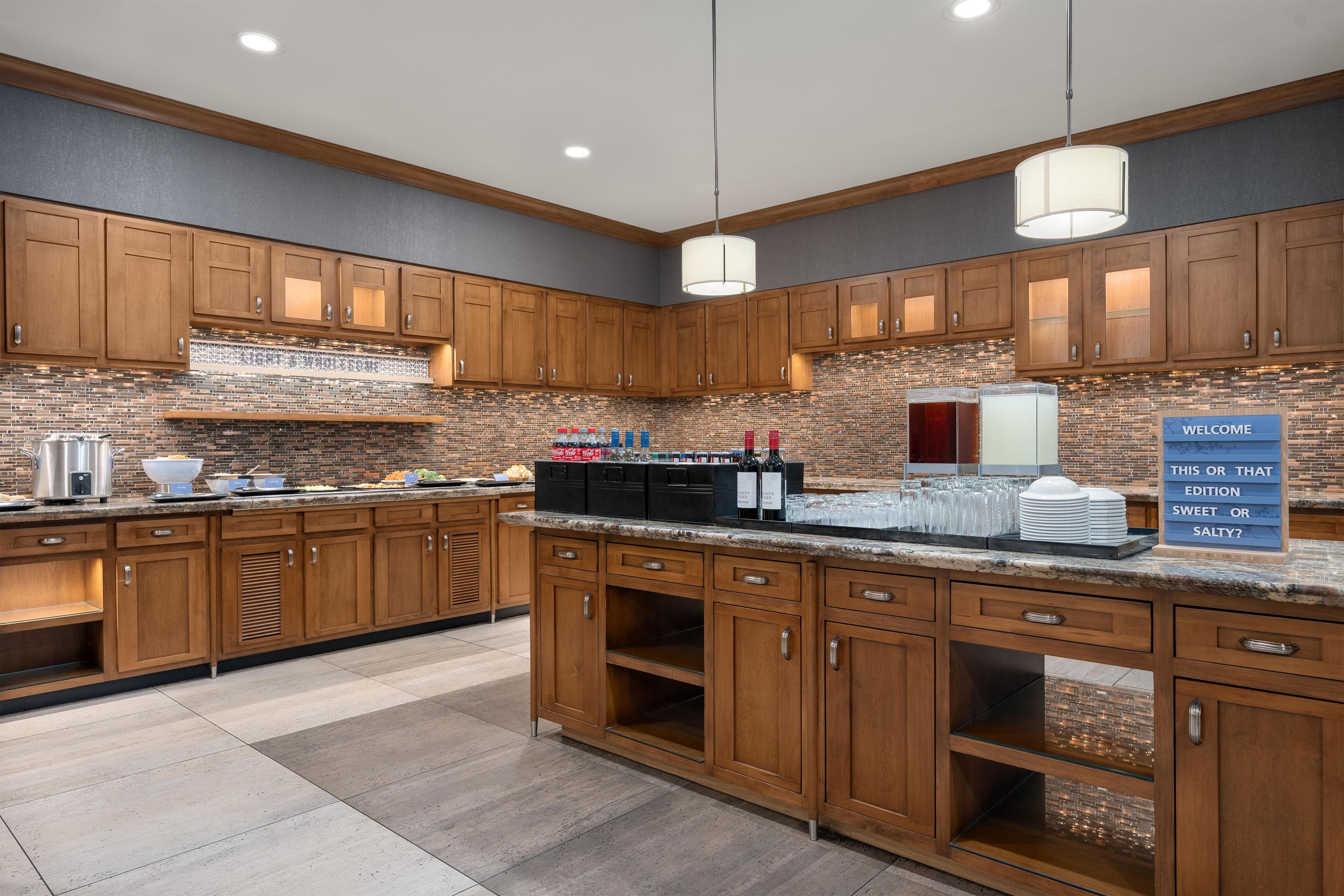 A modern kitchen with wooden cabinets, a brick backsplash, and a buffet setup.