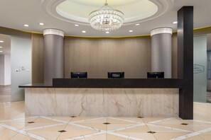 Un mostrador de recepción de hotel con encimera de mármol, una araña y una pared con textura.