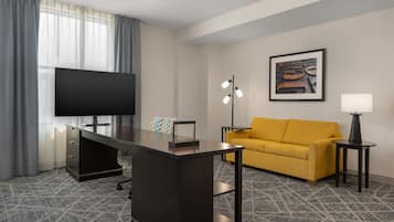 Une chambre d’hôtel équipée d’un bureau, d’un canapé, d’une télévision, d’une œuvre d’art encadrée et d’une lampe.