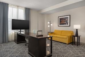 A hotel room with a desk, a sofa, a television, a framed artwork, and a lamp. - Hampton Inn & Suites Cincinnati-Downtown (Cincinnati)